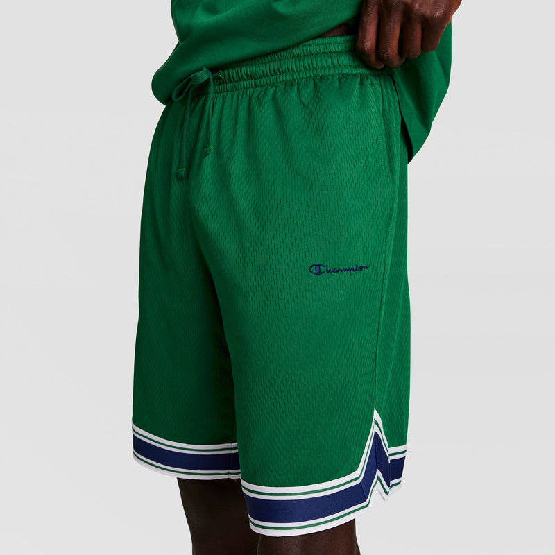 A person wearing green mesh Champion athletic shorts with a white and blue striped trim, standing against a plain light background. Only the lower torso and part of the hand are visible.