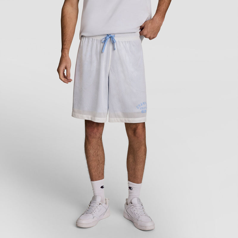 A person wearing a white T-shirt, Champion 9" Gridiron Double Layer Short with C Logo in light blue mesh with a blue drawstring, white socks, and white sneakers stands against a plain white background.