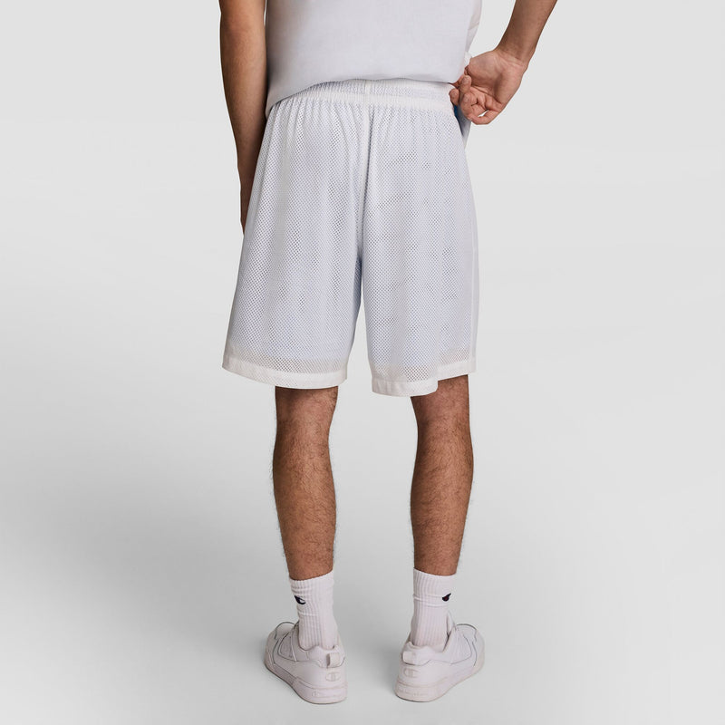 A person faces away, wearing a white shirt, Champion 9" Gridiron Double Layer Short with C Logo, white socks, and white sneakers against a plain white background.