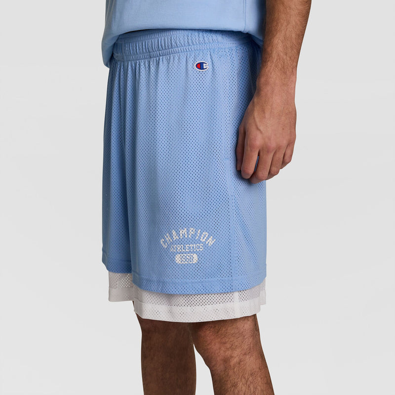 A person wears Champion 9" Gridiron Double Layer Shorts with the C Logo near the hem in light blue, shown waist to knee against a plain background.