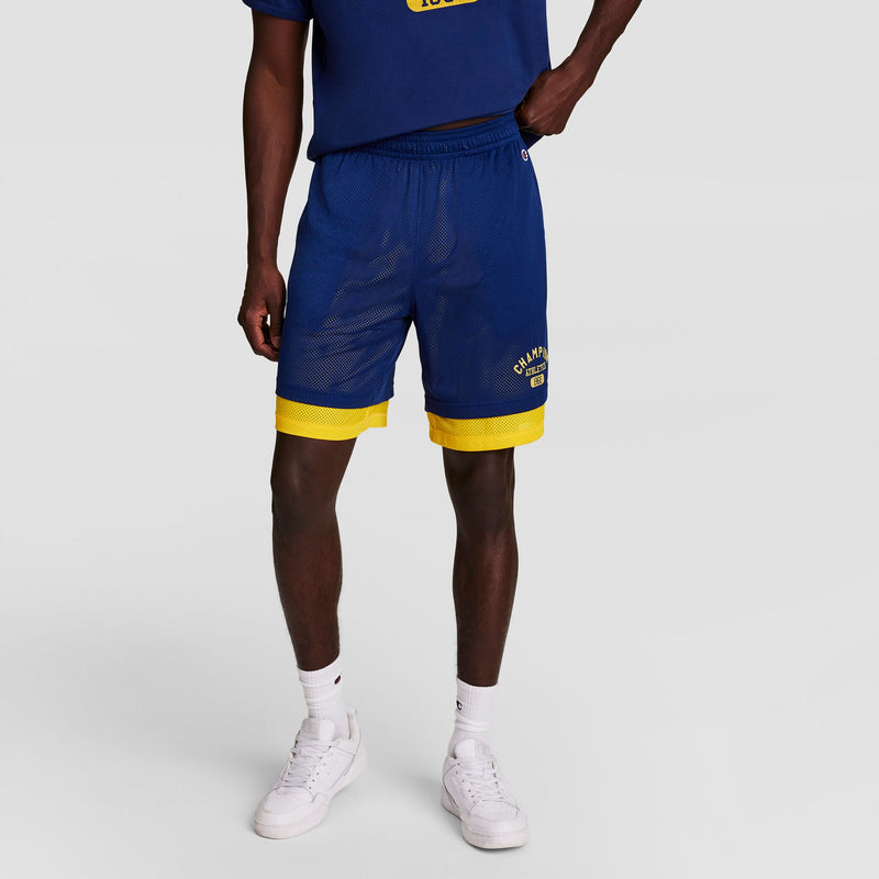 A person stands against a light gray background wearing blue athletic shorts with yellow trim, a matching blue T-shirt, white socks, white sneakers, and the Champion Powerblend Full-Zip Hoodie, C Logo - Big & Tall.