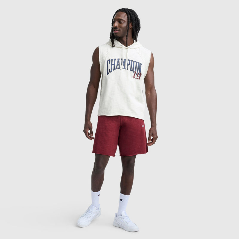 A man wearing a sleeveless white Champion hoodie, 9" Modern Retro Washed Shorts with the C Logo in red, white crew socks, and white sneakers stands against a plain light gray background.