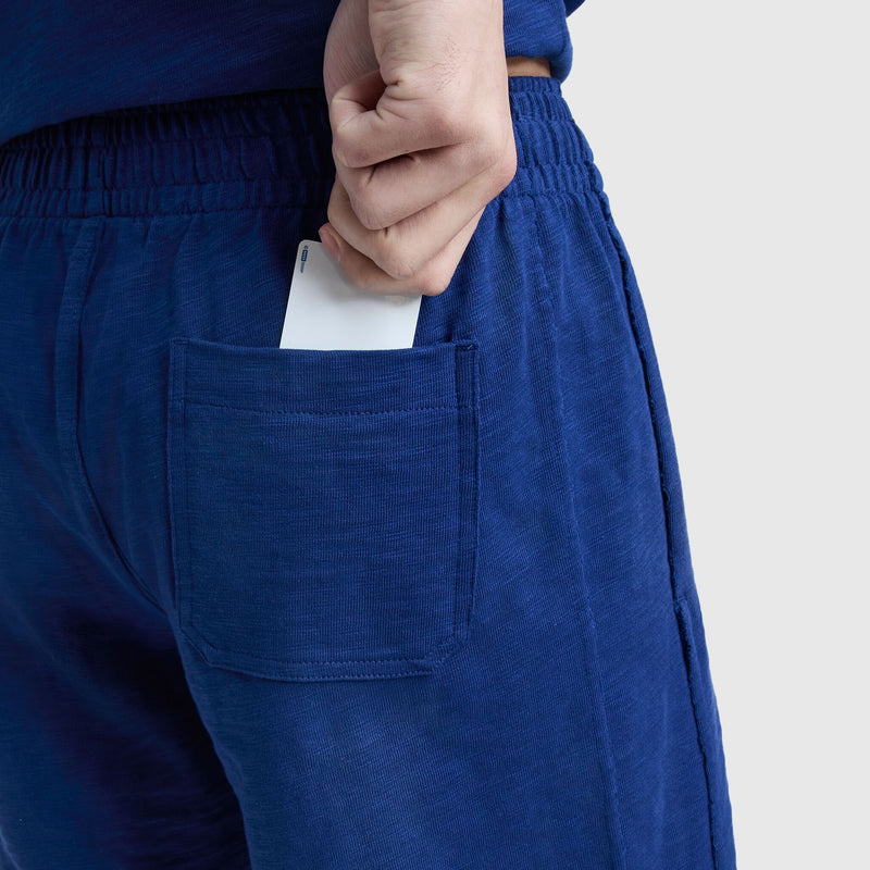 Someone in Champion 9" Modern Retro Washed Shorts with a C Logo and elastic waistband slides a white card into the back pocket against a plain, light background.