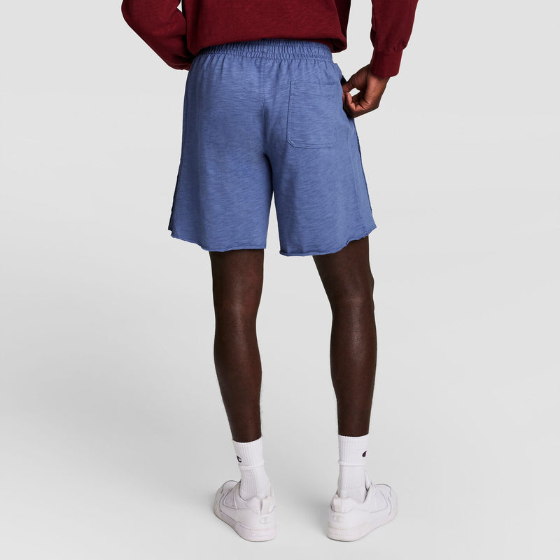 A person in a maroon long-sleeve shirt, Champion 9" Modern Retro Washed Shorts (C Logo) in light blue, white crew socks, and white sneakers stands facing away, highlighting the back of their outfit against a plain light background.