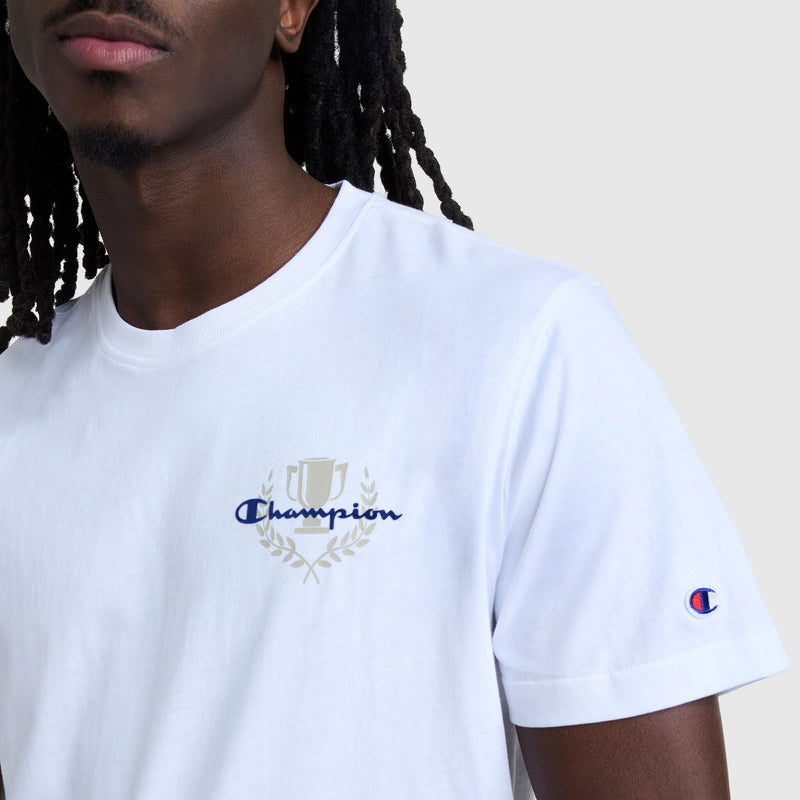 A person with long hair and dark skin wears the Champion Club Graphic T-Shirt, C Logo by Champion. It's white, 100% cotton, golf-inspired, with a trophy and laurel over "Champion" on the chest and the logo on the sleeve.