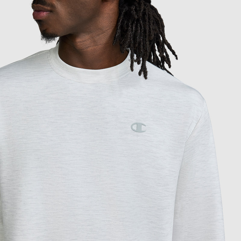 A man is shown from the shoulders up against a plain background, wearing the Champion Sport Long Sleeve Crewneck with C Logo—a white textured athletic sweatshirt featuring a small Champion logo on the left chest.
