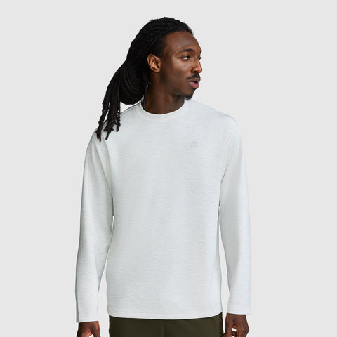 A man with long dreadlocks wears a Champion Sport Long Sleeve Crewneck, C Logo in light gray and dark pants, standing against a plain light gray background while looking to his left.