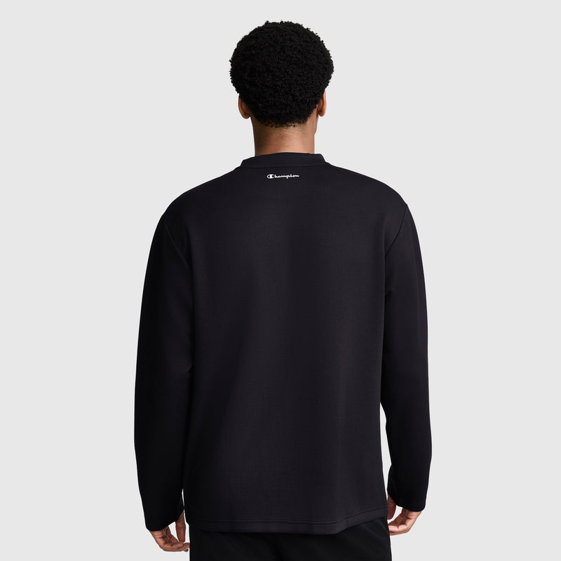 A person stands facing away, wearing a black Champion Sport Long Sleeve Crewneck, C Logo, with the brand's logo featured at the top center of the back against a plain gray background—ideal athletic wear that combines performance and style.