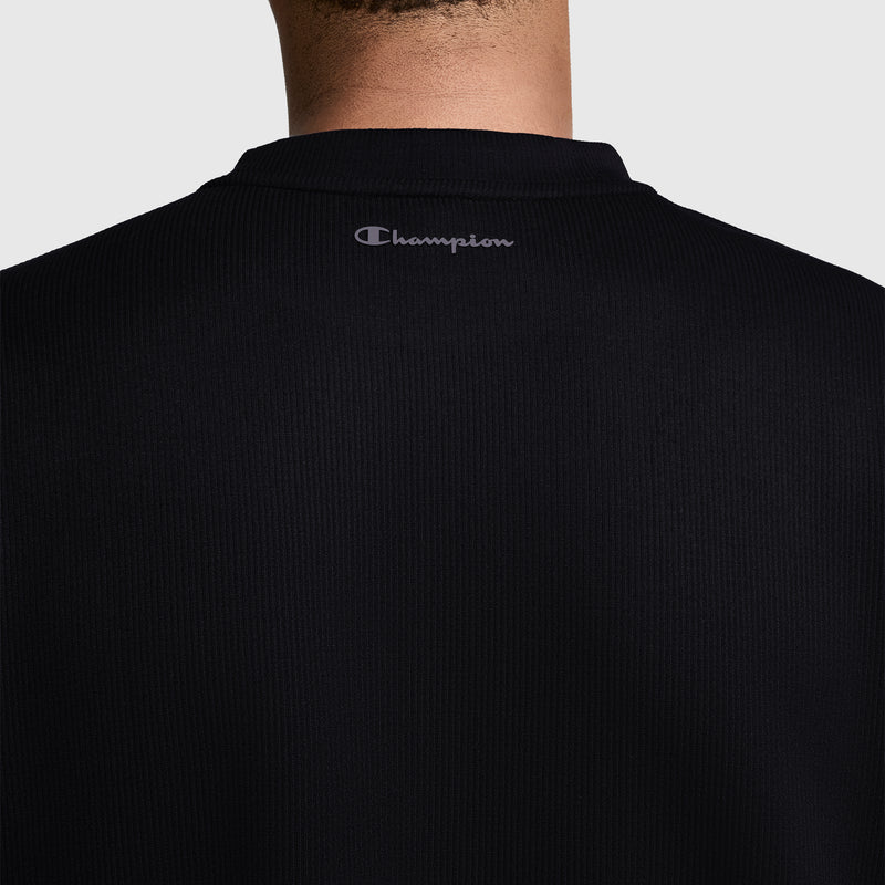 A back view of a person wearing the Champion Sport Long Sleeve Crewneck, C Logo in black, featuring the gray Champion logo near the neck. The athletic top stands out against a plain light gray background.