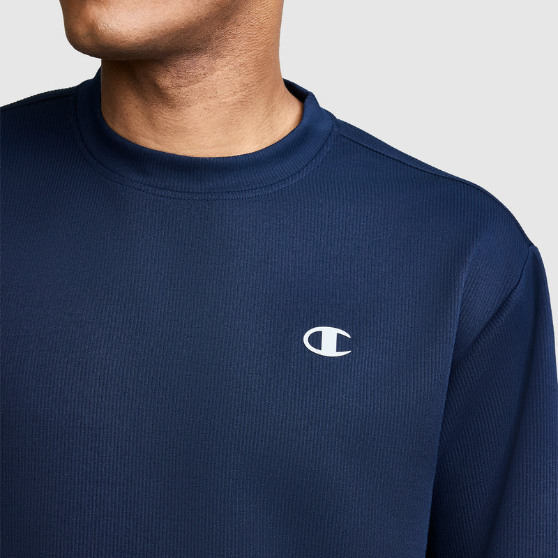 A person wearing a navy blue Champion Sport Long Sleeve Crewneck, C Logo sweatshirt, with the upper chest and neck visible, featuring an athletic crewneck and the Champion logo on the left side.