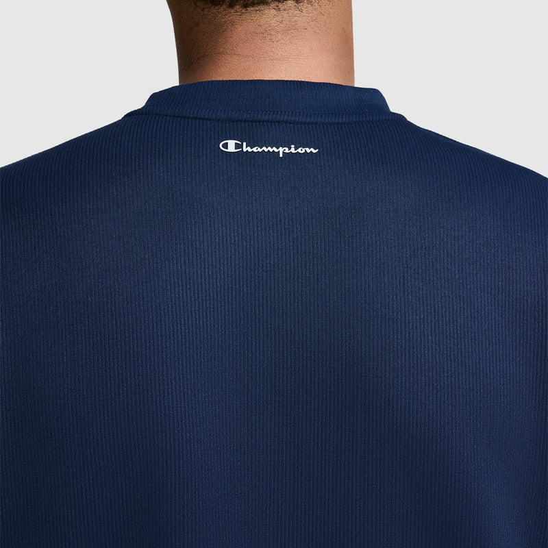 A back view of a person wearing the Champion Sport Long Sleeve Crewneck, C Logo in navy blue ribbed fabric, featuring the white Champion "C" logo printed near the collar. The athletic crewneck provides a comfortable fit, with the wearer's neck and upper back visible.