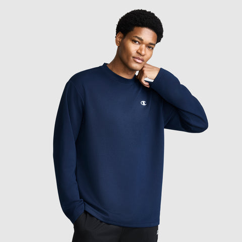 A person wearing a Champion Sport Long Sleeve Crewneck with the C Logo in navy blue stands against a plain light gray background, one hand touching their chin and the other in their pocket.