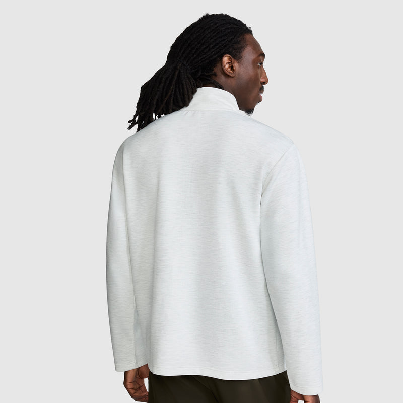 A man with long braided hair wears a Champion Sport Long Sleeve 1/4 Zip Mockneck featuring the C Logo in light gray and dark pants, standing and facing away from the camera against a plain gray background.