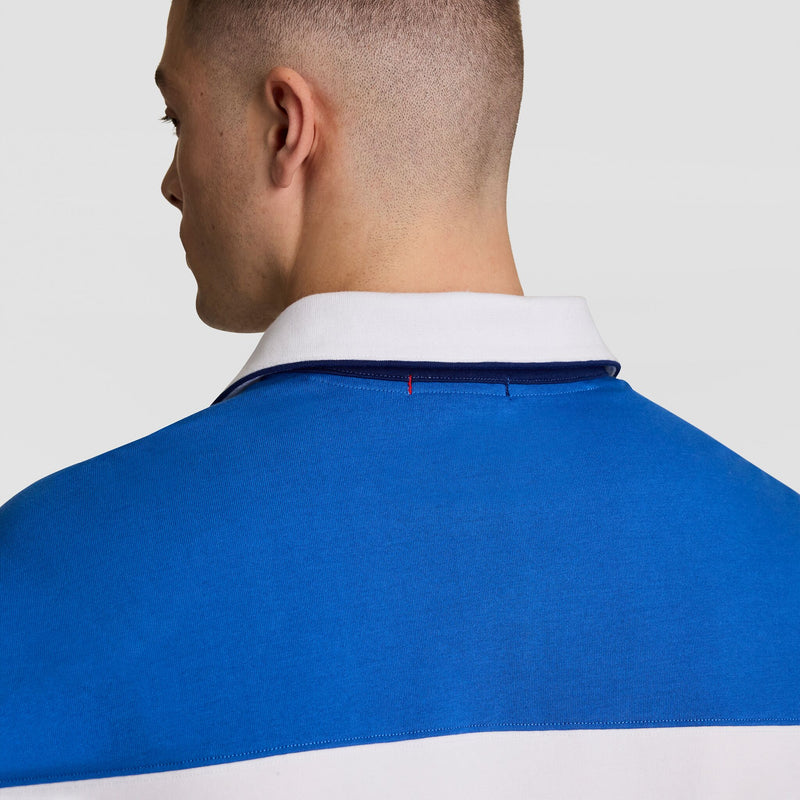 Seen from behind, a person with short hair wears the Champion Gridiron Blocked Long Sleeve Rugby with script logo, featuring a white collar and blue upper section, standing out against a plain, light-colored background.