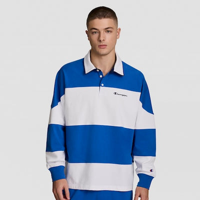 A young man stands facing forward, wearing a blue and white striped, long-sleeve rugby shirt with a collar and the Champion logo on the chest. The background is plain and light-colored.