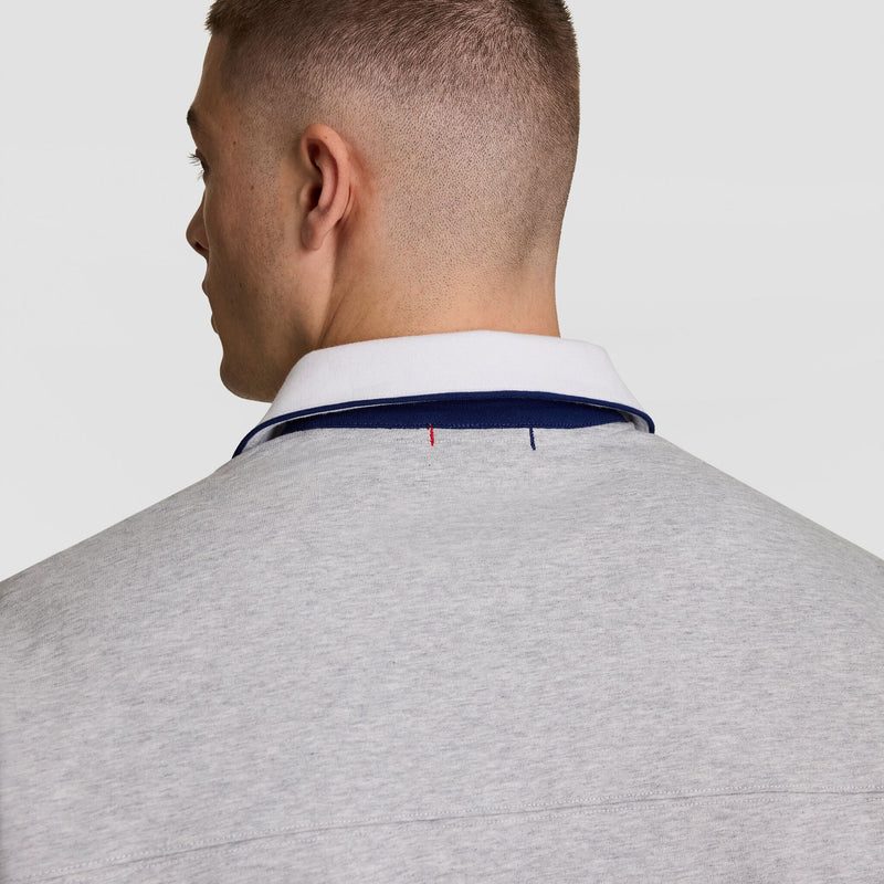 A person with short brown hair is shown from behind, wearing a light grey collared shirt with a white collar and a navy trim. The background is plain and light-colored.