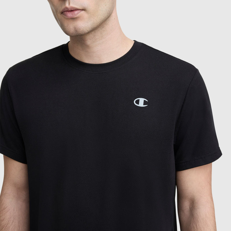 A person wears a Champion Sport Crewneck T-Shirt, Script Logo, in plain black with a small white script logo on the left chest, shown from shoulders to above the elbow against a light gray background.