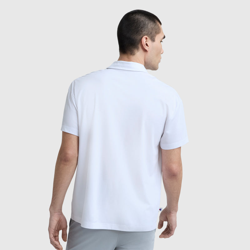 A man with short dark hair is seen from behind wearing a Champion Sport Polo, C Logo, and light gray pants, standing against a plain light gray background for a refined athletic look.