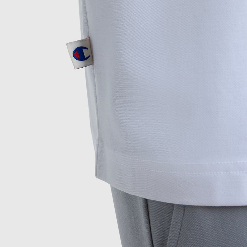 Detail of the Champion Sport Polo, C Logo in white, featuring a small logo tag on the side and styled with light gray pants for an athletic look against a plain white background.