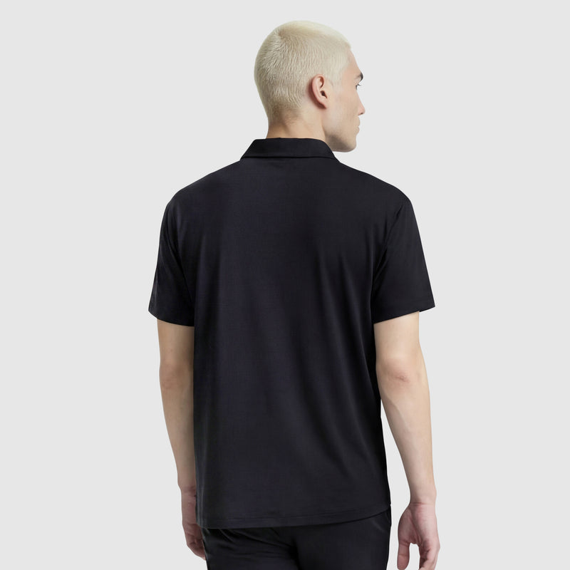 A person with short, bleached blonde hair is seen from behind wearing a Champion Sport Polo, C Logo in black with an athletic style against a light gray background.