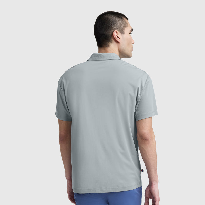 A man with short dark hair is seen from behind, wearing the Champion Sport Polo, C Logo in light gray and blue pants, standing against a plain background.