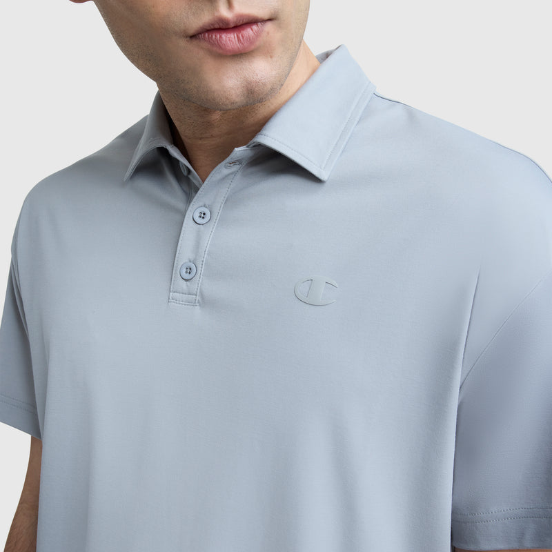 A man wears the Champion Sport Polo featuring a light gray color, three buttons, and a subtle C logo embroidered on the chest, shown from shoulders to mid-torso against a plain background.