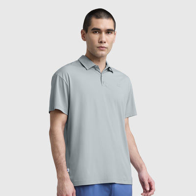 A man with short dark hair wears a light gray Champion Sport Polo, C Logo, and blue pants. He stands against a plain white background with a neutral expression and his arms relaxed by his sides.