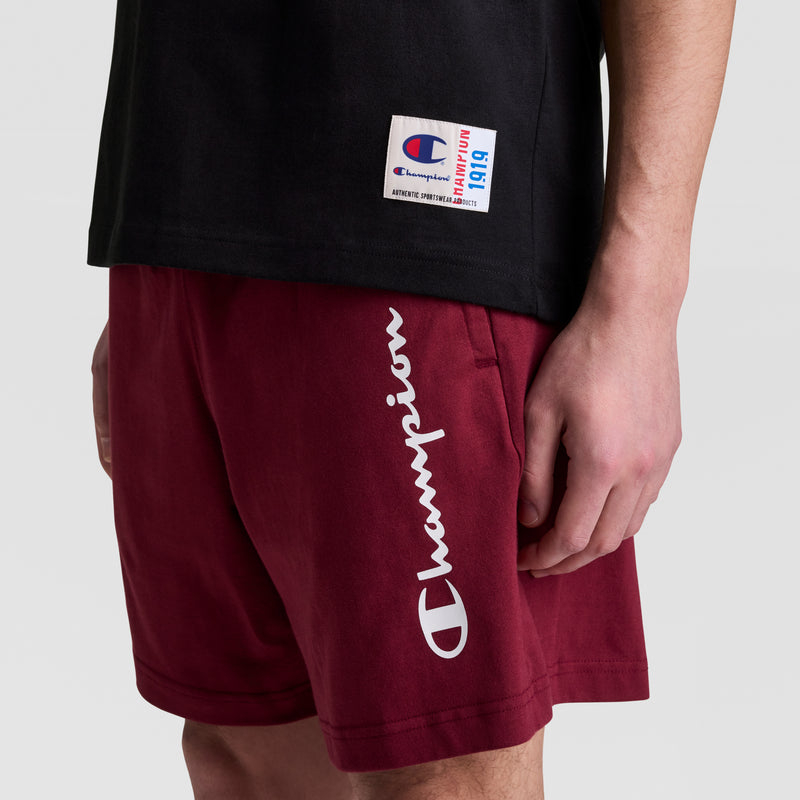 A person wearing a black Champion sleeveless hoodie with a C logo and maroon Champion shorts with white logos, shown from the waist down against a plain background.