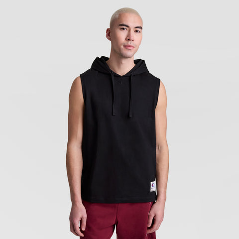 A person with short blond hair wears a Champion Sleeveless Hoodie, C Logo, featuring a front pocket and drawstrings, paired with maroon shorts, standing against a plain light gray background.