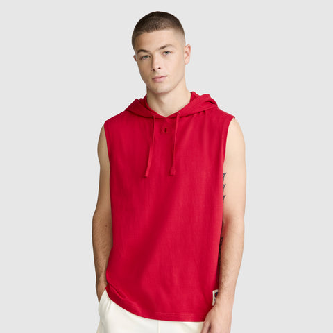 A young man with short hair wears the Champion Jersey Sleeveless Hoodie, C Logo, crafted from soft ring-spun cotton, along with white pants, standing against a plain light gray background.