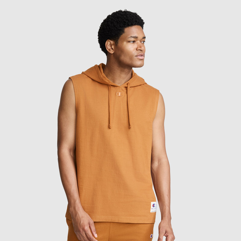 A man wearing the Champion Jersey Sleeveless Hoodie, C Logo in orange, crafted from soft ring-spun cotton and paired with matching pants, stands against a plain light background looking to the side with a neutral expression.