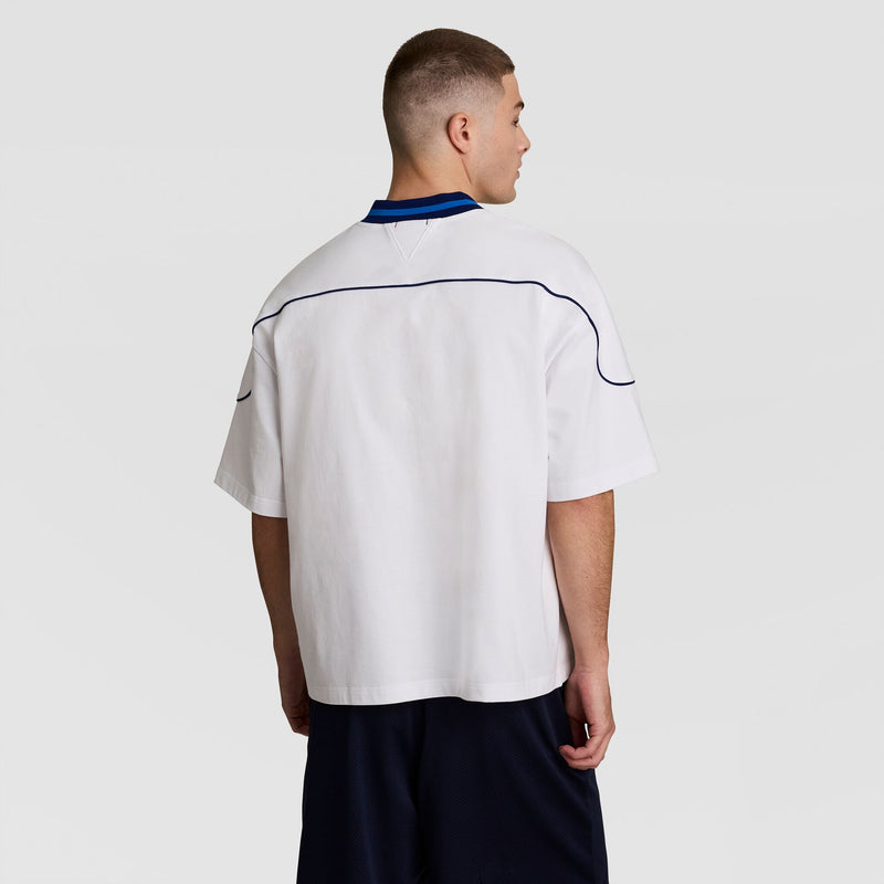 A person with short hair wears the Champion Gridiron Football Jersey, Script Logo, pairing it with dark shorts for a vintage athletic look while facing away from the camera against a plain light background.