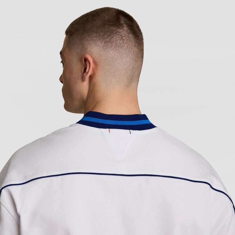 A person with short brown hair is seen from behind wearing the Champion Gridiron Football Jersey, Script Logo, featuring a white base with blue striped collar and blue shoulder piping, set against a plain light background.