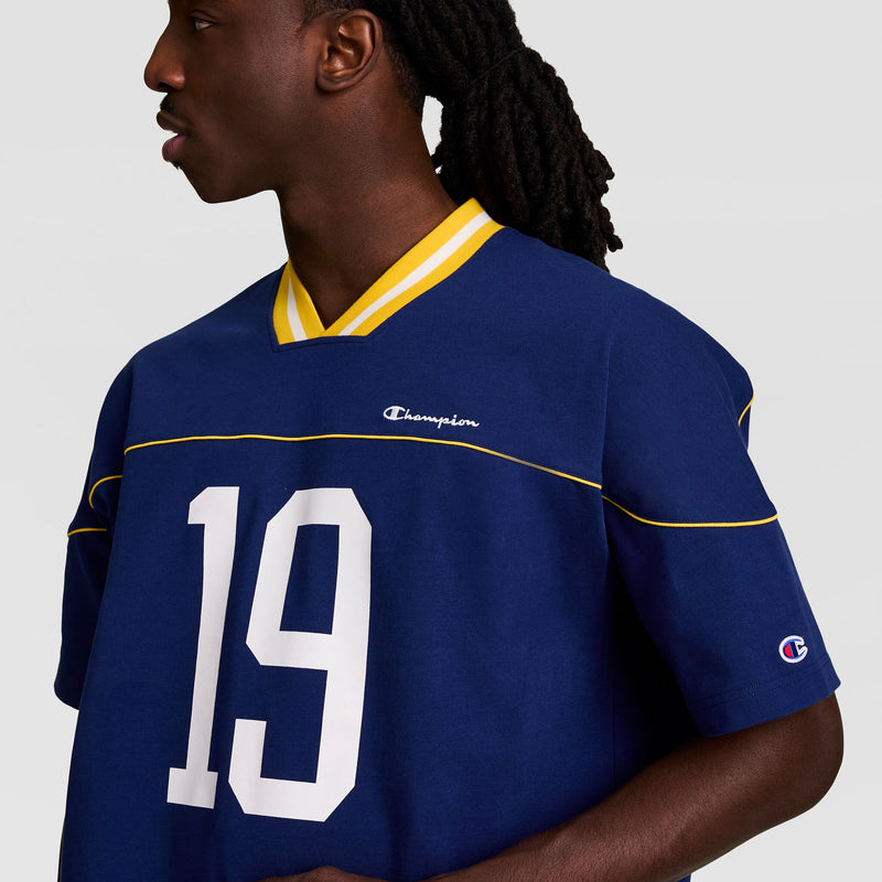 A person wearing the Champion Gridiron Football Jersey, Script Logo—blue with yellow trim and white number 19—stands against a plain light background.