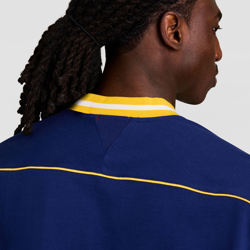 Seen from behind, a person with long, braided hair wears the Champion Gridiron Football Jersey, Script Logo—featuring blue fabric and yellow-white collar trim—set against a plain, light background for a vintage athletic look.
