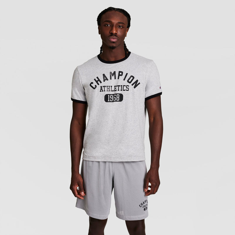 A man wears a light gray Champion Gridiron Reversible T-Shirt with the C Logo and matching gray shorts, standing against a white background and looking directly at the camera with a neutral expression.