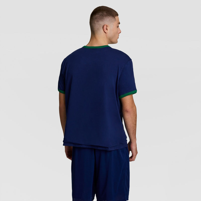 A man faces away from the camera, wearing the Champion Gridiron Reversible T-Shirt (C Logo) in navy with green trim and matching shorts, set against a plain light gray background.