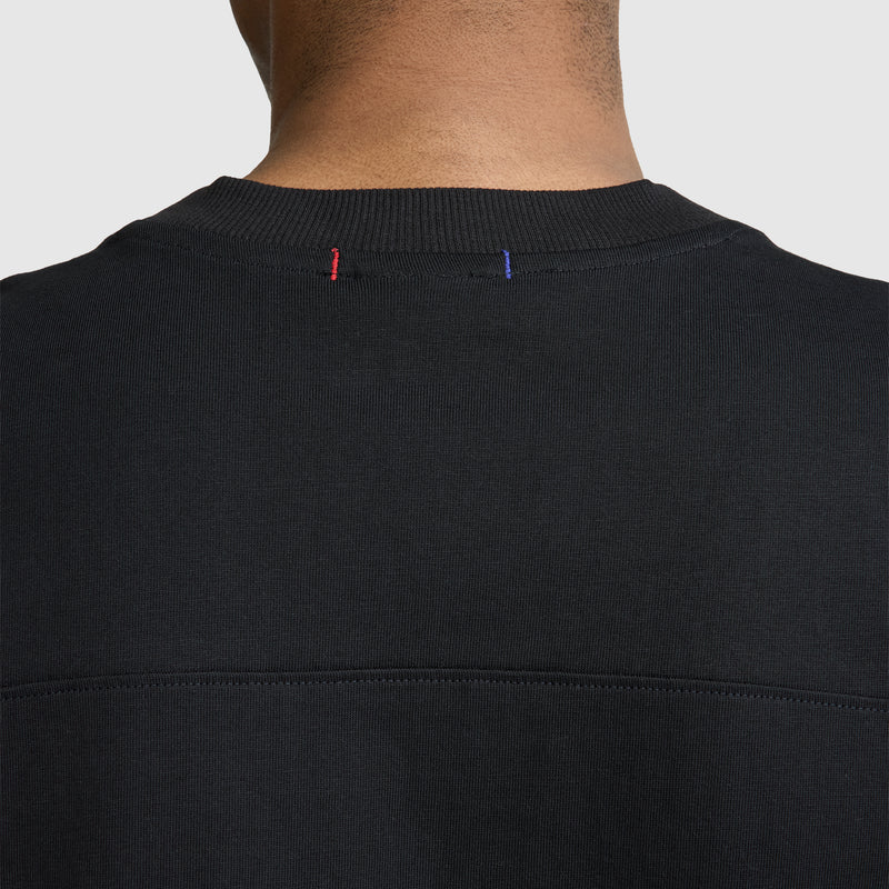 Back view of a person wearing the Champion Short Sleeve Boxy T-Shirt with Embroidered Script Logo in black, highlighting the neckline adorned with subtle red and blue stitches on the collar. Set against a plain, light-colored background, this classic heritage-inspired piece stands out for its relaxed fit and timeless appeal.