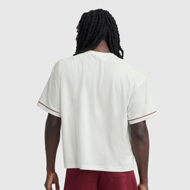 A person with long, dark, twisted hair is seen from behind wearing the Champion Modern Retro Coaches Henley with C Logo and maroon shorts, standing against a plain light gray background.
