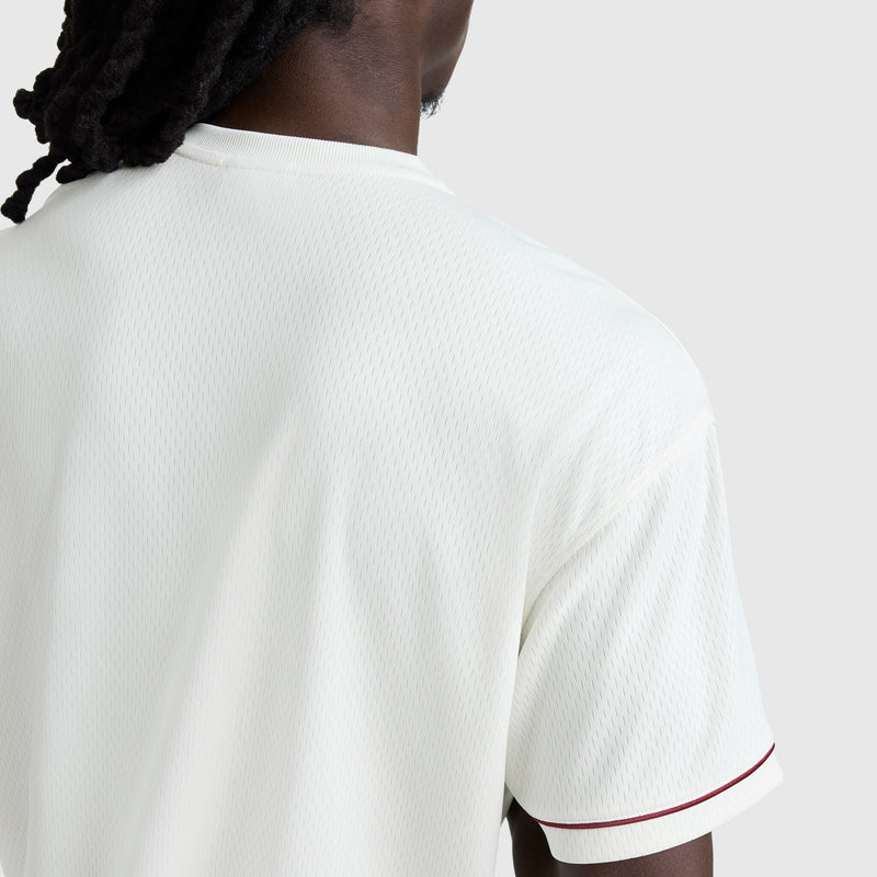 A person with dark twisted hair is seen from the back, wearing the Champion Modern Retro Coaches Henley, C Logo—a white short-sleeve shirt with maroon sleeve trim—against a plain light background.
