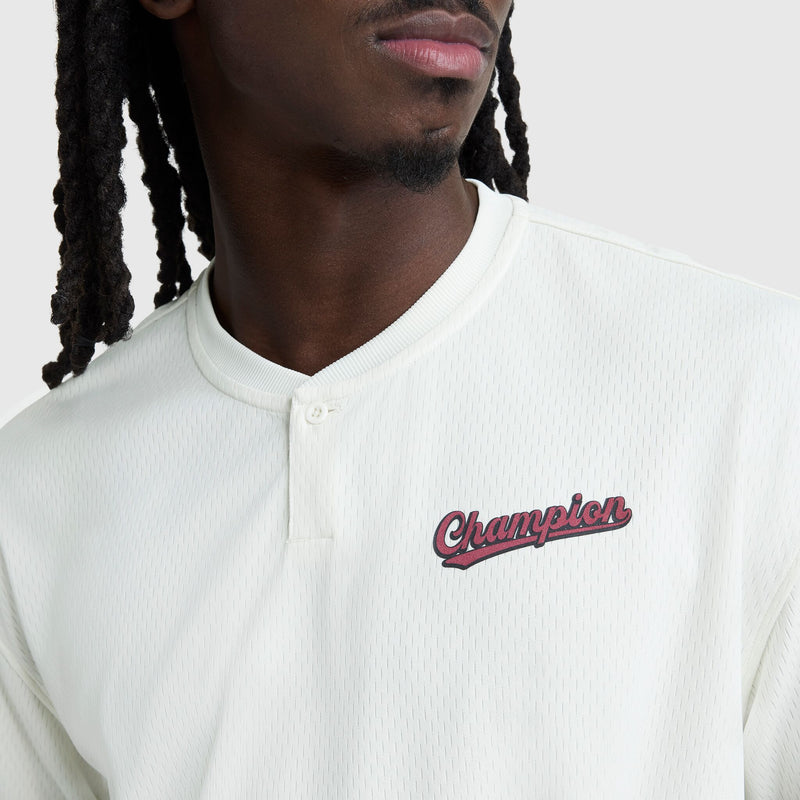 Wearing the Champion Modern Retro Coaches Henley with a red and black C Logo, this person pairs its vintage sport style perfectly with their long, dark braids for a standout look.