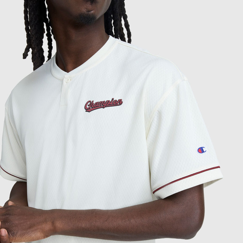 Wearing Champion’s Modern Retro Coaches Henley, C Logo, this person sports a white short-sleeve jersey with maroon trim and classic branding, evoking vintage athletic style. Only the upper body and part of the face are visible against a plain background.