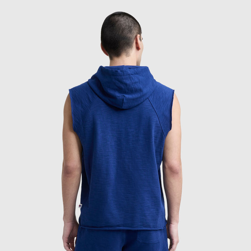A person with short dark hair faces away from the camera, wearing a Champion Modern Retro Washed Sleeveless Hoodie with the C Logo and matching blue shorts against a plain light gray background.