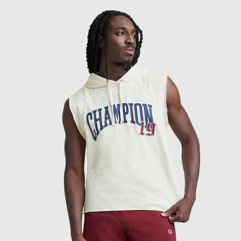 A man with long braids wears the Champion Modern Retro Washed Sleeveless Hoodie with C Logo in off-white, paired with red shorts. He stands against a plain light gray background, looking to the side.