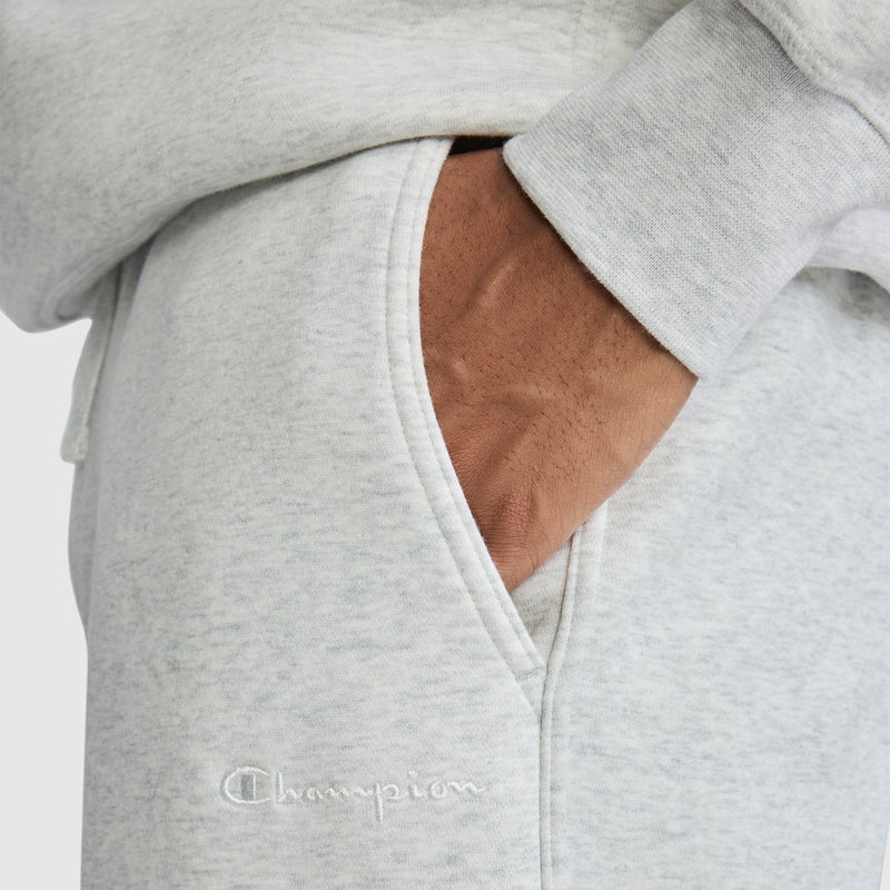 A person wearing light gray "All in a Day's Work Sweatpants" by Champion with their hand in the pocket. The signature Champion logo is embroidered in white near the pocket, adding a classic touch to these essential workwear sweatpants.