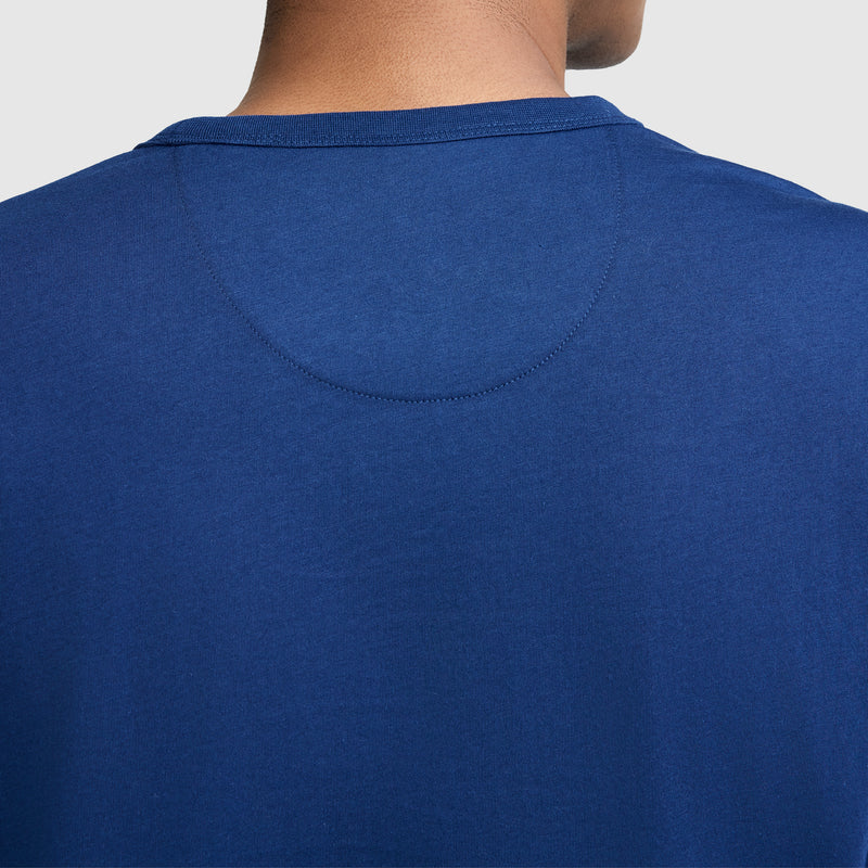 Close-up of the back of a person wearing a Champion Medallion Long Sleeve Graphic T-Shirt, showing the upper portion of the shirt and part of the person's neck against a light background.