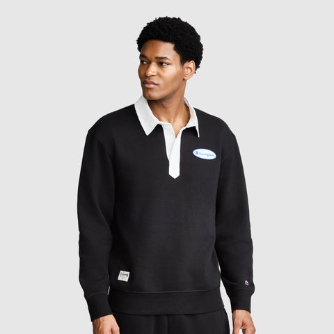 A man wearing the Champion Fleece Rugby shirt in black, featuring a white collar and a small Champion logo on the chest, stands against a plain gray background.
