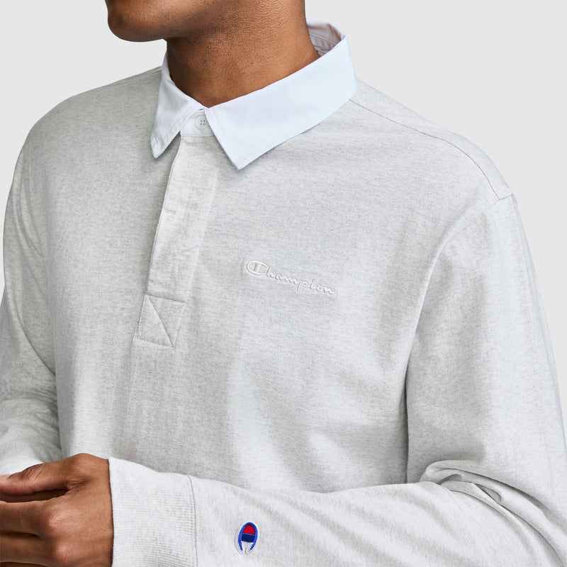 A person wearing the Champion Long Sleeve Rugby Shirt with Twill Collar, featuring a white collar, embroidered C logo on the chest, and the Champion emblem on the sleeve, stands against a plain light background.