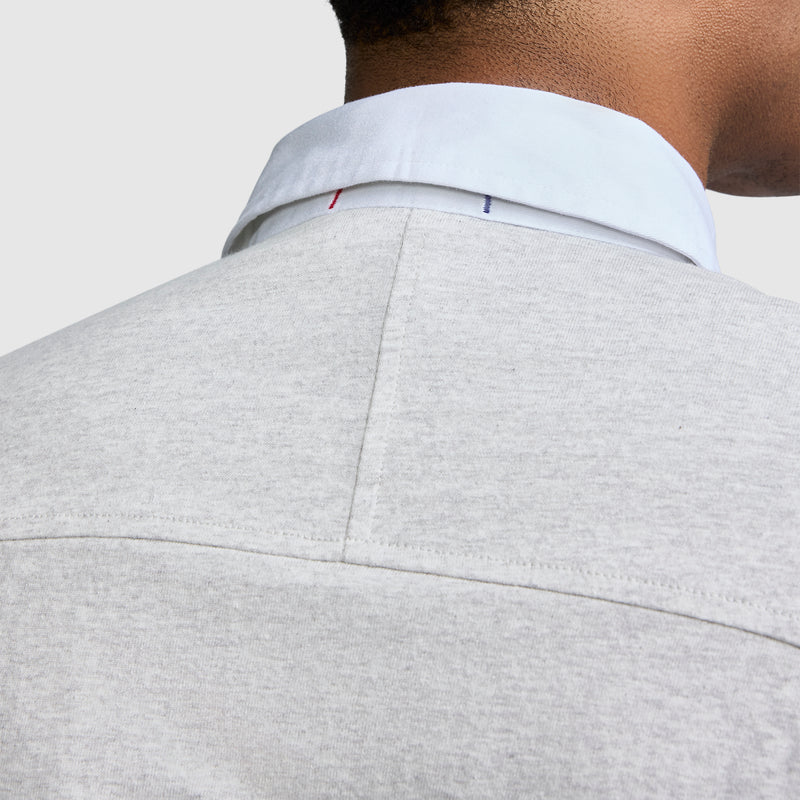 Close-up of the back of a person’s neck and shoulders, wearing the Champion Long Sleeve Rugby Shirt with Twill Collar, featuring a light grey color, white collar, and two small embroidered stitches—one red and one blue—on the back of the collar.