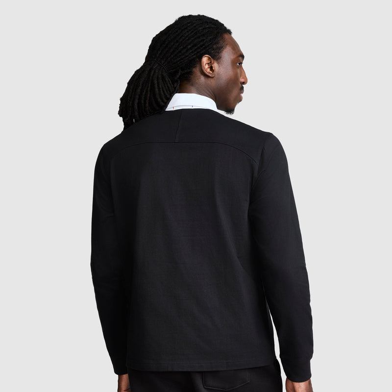 A person with long, dark, braided hair facing away is wearing a black jacket over the Champion Long Sleeve Rugby Shirt with Twill Collar and Embroidered C Logo, featuring a white collar and long sleeves, set against a plain light gray background.